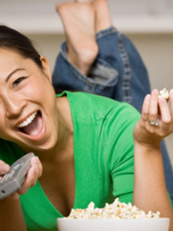 Happy woman laying on floor with bowl of popcorn, remote control